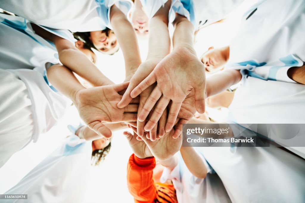 View from below of young female soccer players bringing hands together before game