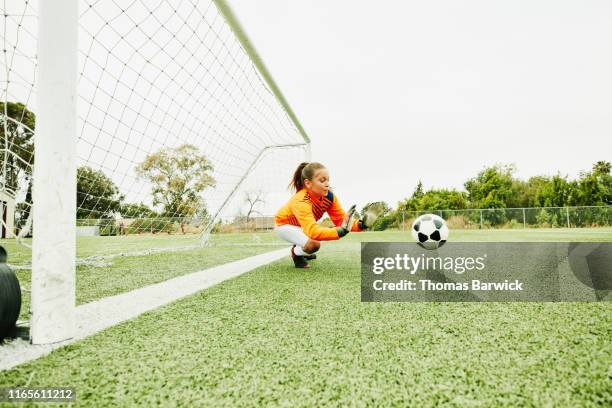 young female soccer goalie diving to stop shot - goal photos et images de collection