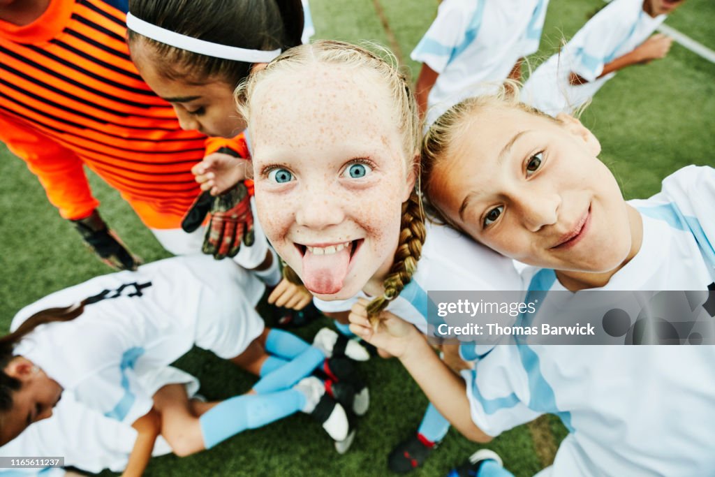 Young female soccer player sticking out tongue and playing with teammates after game