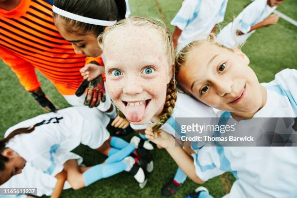 young female soccer player sticking out tongue and playing with teammates after game - children sport foto e immagini stock
