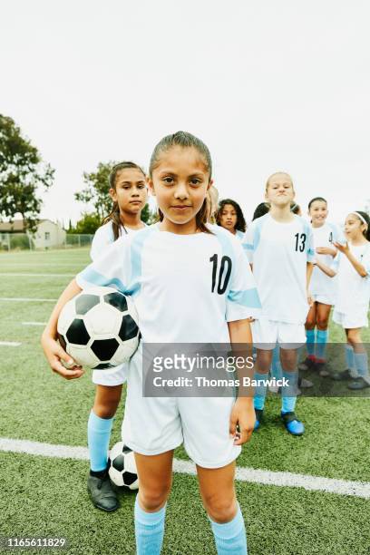 portrait of young female soccer player holding ball and standing in front of teammates - nosotroscollection stockfoto's en -beelden
