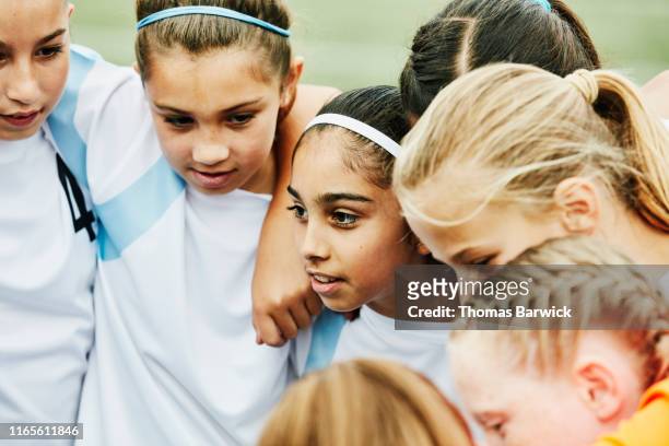 Young female soccer players with arms around each other huddled together before game