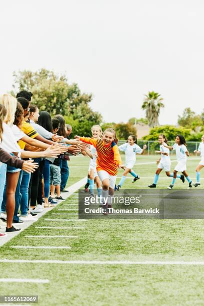 young female soccer player running though line of high fives with families on sidelines after game - fan appreciation day stock-fotos und bilder