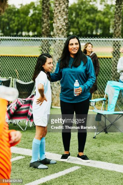 Smiling mother and young female soccer player in discussion on sidelines after game