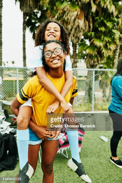 smiling young female soccer player riding piggy back on older sister after game - teenager playing football stock pictures, royalty-free photos & images