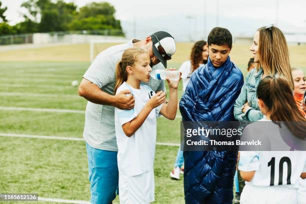 father embracing young female soccer player drinking water after game - 13 year old girls in shorts stock pictures, royalty-free photos & images