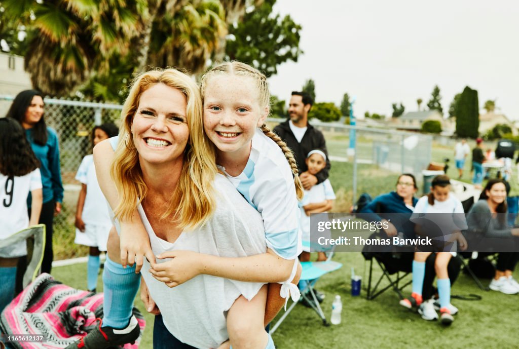 Smiling mother giving daughter piggy back ride on sidelines after soccer game