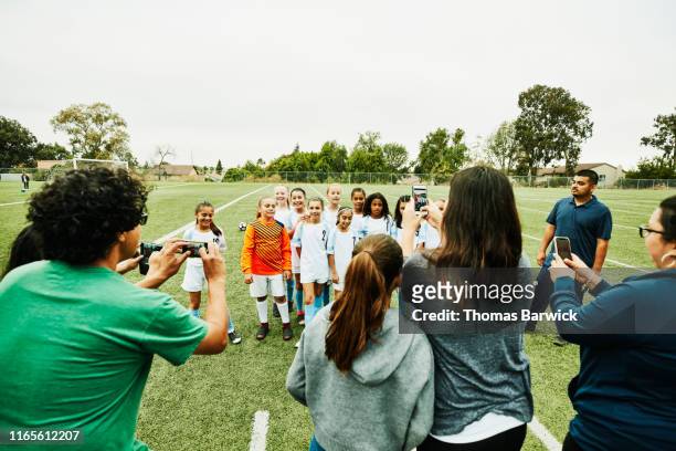 parents taking pictures with smartphones of young female soccer team on field after game - soccer mum stock pictures, royalty-free photos & images