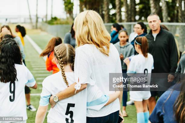 mother embracing young female soccer player on sidelines after game - voetbalcompetitie sportevenement stockfoto's en -beelden