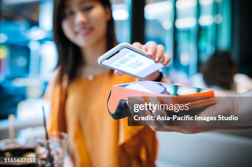 Asian young woman paying with smartphone in a cafe. Asian young woman paying with smartphone in a cafe.