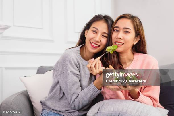 two young asian friends or or lesbian couple enjoy eating mix salad and spending time together in living room at home, lgbt and homosexual lifestyle concept - asian lesbians kiss stock pictures, royalty-free photos & images
