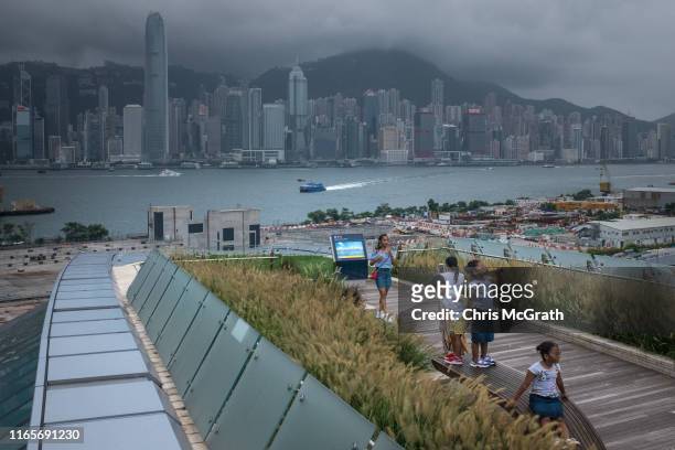 People pose for photographs in front of the Hong Kong skyline from the rooftop of the West Kowlo on Train stati on on July 9, 2019 in Hong Kong,...