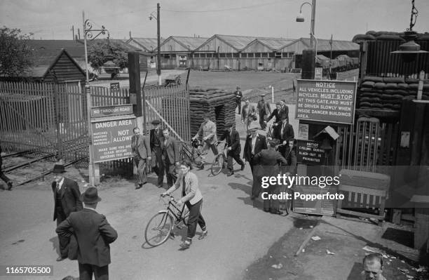 View of both male and female munitions workers walking out of a gate with bicycles on their way home for lunch at the end of a morning shift at the...