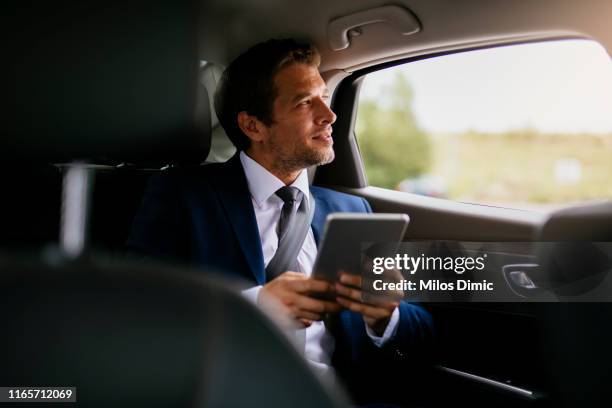 schöne geschäftsmann sitzt mit digitalen tablet auf dem rücksitz des auto-lager foto - business person ipad travel stock-fotos und bilder