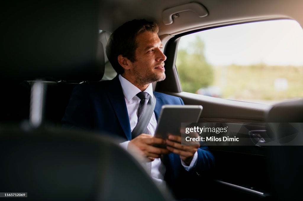 Handsome businessman sitting with digital tablet on the backseat of the car stock photo