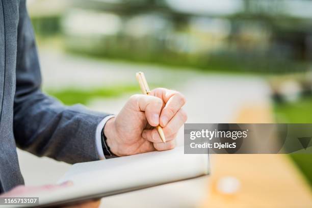 young businessman taking notes outdoors hand close up. - dandy diary stock pictures, royalty-free photos & images