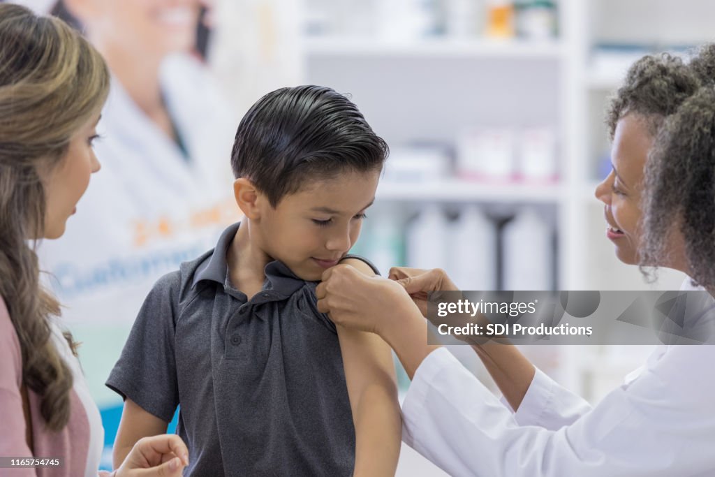 Le garçon regarde en tant que pharmacien applique le bandage adhésif après projectile