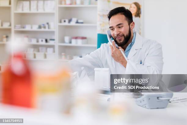 pharmacist holds phone while checking medications - pharmacist stock pictures, royalty-free photos & images