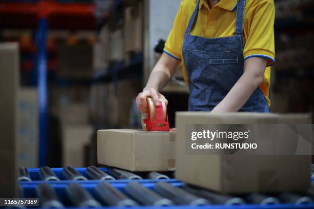 warehouse worker sealing cardboard box on conveyor belt - inventory management stock pictures, royalty-free photos & images