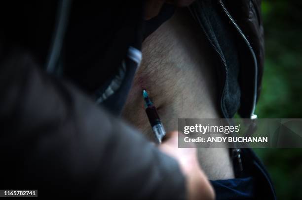 Graphic content / A drug addict injects cocaine into a vein in his leg in a small wooded area used by addicts to take drugs near Glasgow city centre,...