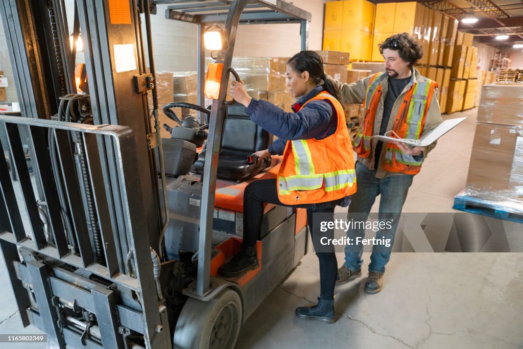 Ett industri lager arbetsplatssäkerhet ämne. En säkerhets handledare eller chef utbildning en ny anställd på gaffeltruck säkerhet.