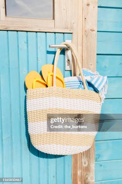 beach bag with towel and flip-flops hanging at a door of a blue painted wooden house - tote bags stock pictures, royalty-free photos & images