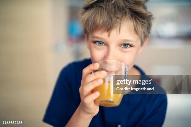 netter kleiner junge, der ein glas orangensaft trinkt - drinking juice stock-fotos und bilder