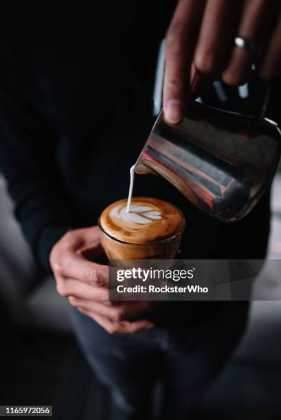 man in house robe pouring steamed milk into cup of cappuccino for latte art. - latte art stock pictures, royalty-free photos & images