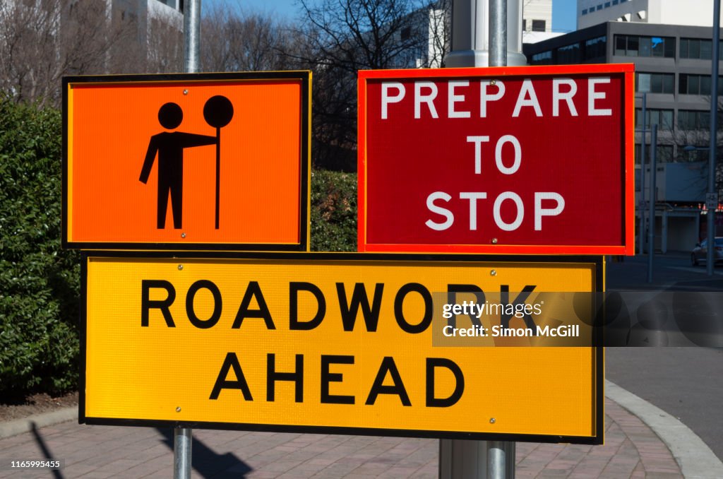 Signs warning drivers to prepare to stop and heed the worker with a stop sign because of roadwork ahead