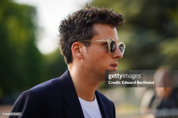 Guest wears sunglasses, a white t-shirt, a navy blue jacket, outside Miu Miu Club 2020, on June 29, 2019 in Paris, France.