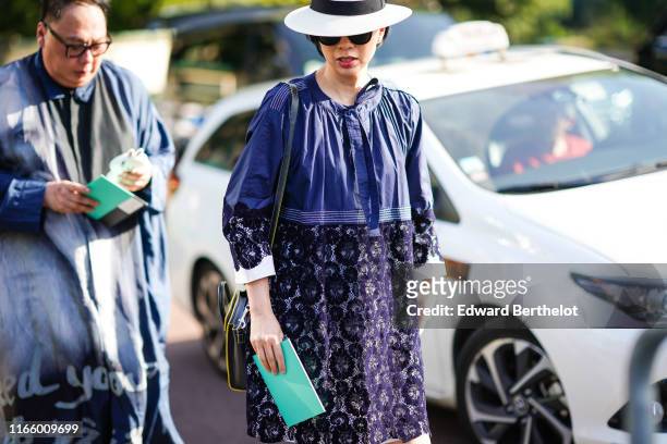 Guest wears sunglasses, a white hat, a purple lace flowing gathered dress, a yellow trimmed black bag, outside Miu Miu Club 2020, on June 29, 2019 in...