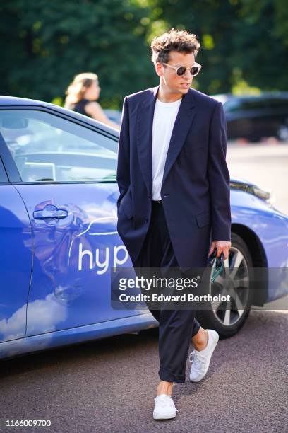 Guest wears sunglasses, a white t-shirt, a navy blue jacket, navy blue cuffed pants, white sneakers, outside Miu Miu Club 2020, on June 29, 2019 in...