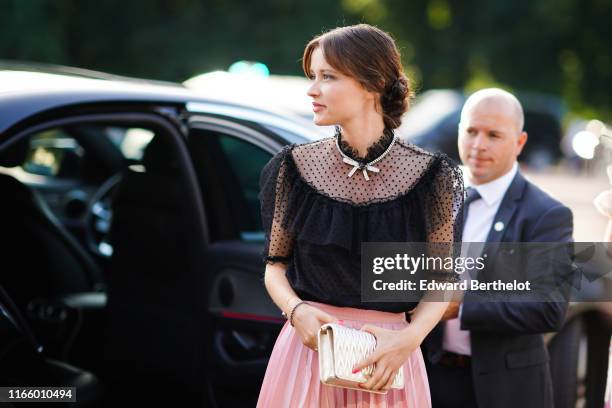 Guest wears a partly transparent black plumetis frilly top, a rhinestone necklace, a pink pleated skirt, a lustrous golden color Miu Miu bag, outside...