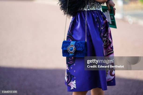 Guest wears a purple dress with printed features, a blue bag, outside Miu Miu Club 2020, on June 29, 2019 in Paris, France.