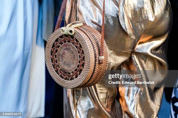 Guest wears a shiny golden jumpsuit, a round woven straw canteen bag, outside the "Scandal A Paris" : Jean-Paul Gaultier's New Fragance Launch Dinner...