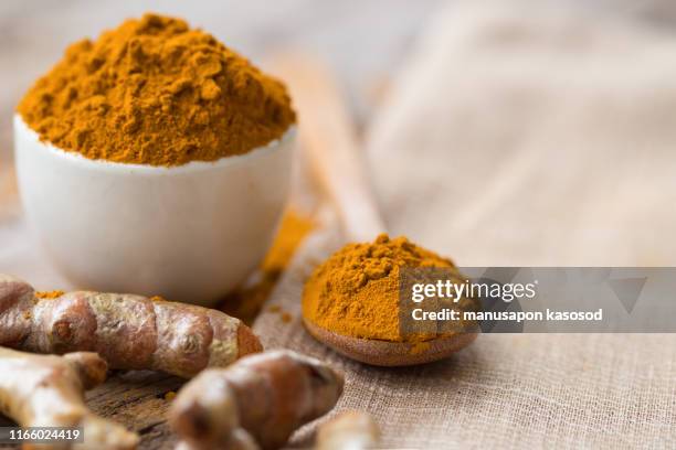 turmeric powder and fresh turmeric in wood bowls on wooden table. - tumeric stock pictures, royalty-free photos & images