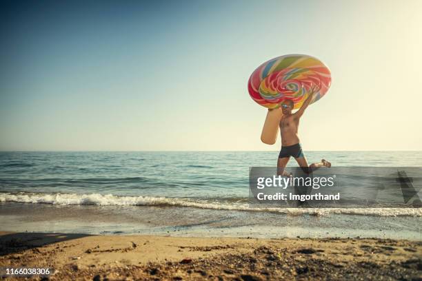 gelukkige man springen op het strand met een gigantische opblaasbare lollipop. - lollipop man stockfoto's en -beelden