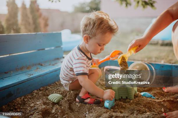 child plays with his single mother in the sandbox - family garden play area stock pictures, royalty-free photos & images