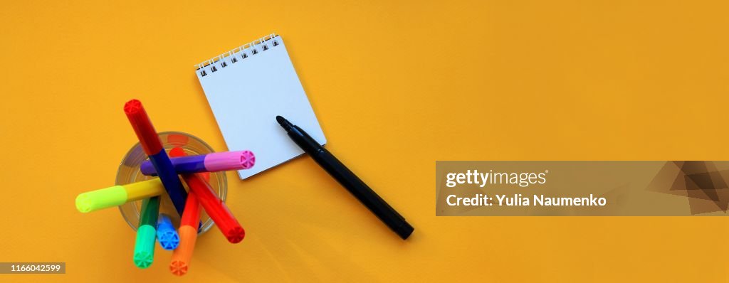 Top view banner of felt-tip pens and blank notepad on yellow background. Copy-spase, concept of the educational process, study at school.