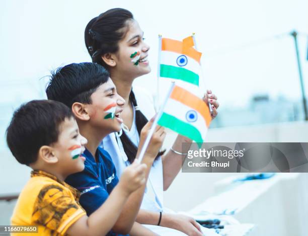 happy indian teenager girl with two little boys holding national indian flag with pride - indian national flag stock pictures, royalty-free photos & images