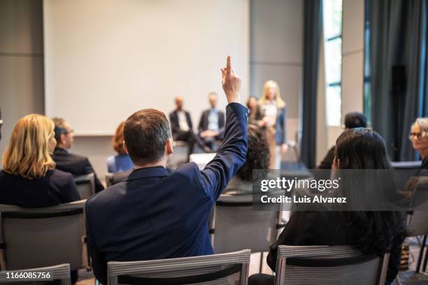 businessman raising hand to ask question in seminar - débat photos et images de collection