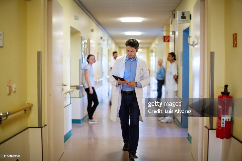 Doctor with a digital tablet walking through hospital corridor