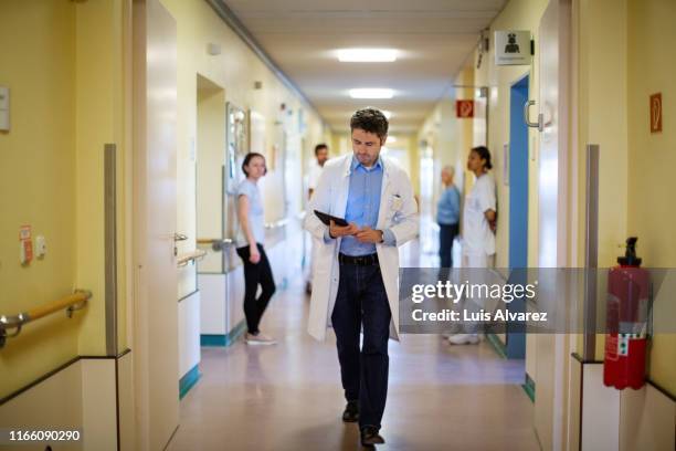 doctor with a digital tablet walking through hospital corridor - acute care stock pictures, royalty-free photos & images