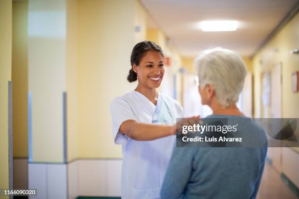 nurse consoling a senior woman in hospital hallway - enfermeira - fotografias e filmes do acervo