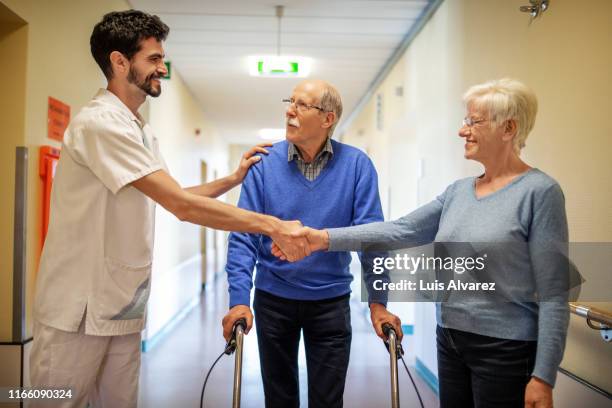 woman appreciating the support of a carer during her husbands rehab - couple shaking hands with doctor stock-fotos und bilder