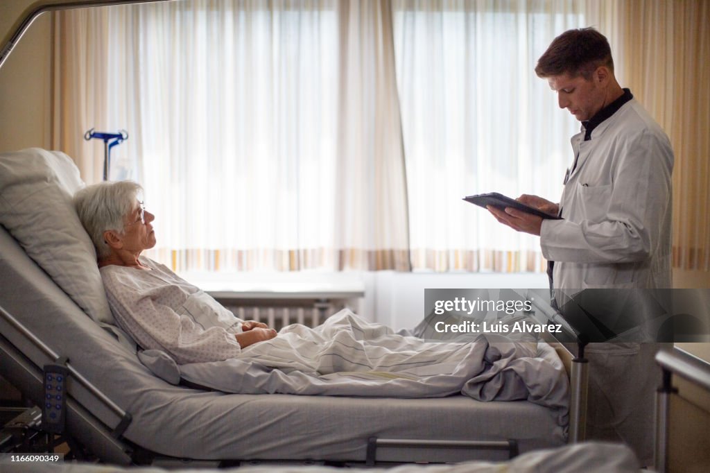Male doctor visiting senior patient in hospital ward