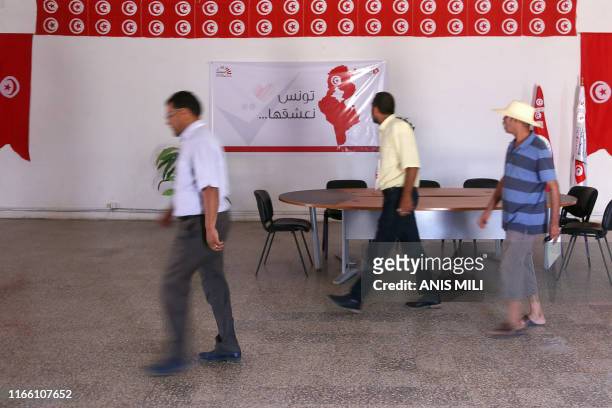 Men walk past a banner reading "Tunisia, we adore it" inside a branch of the Independent High Authority for Elections on August 15 in the central...