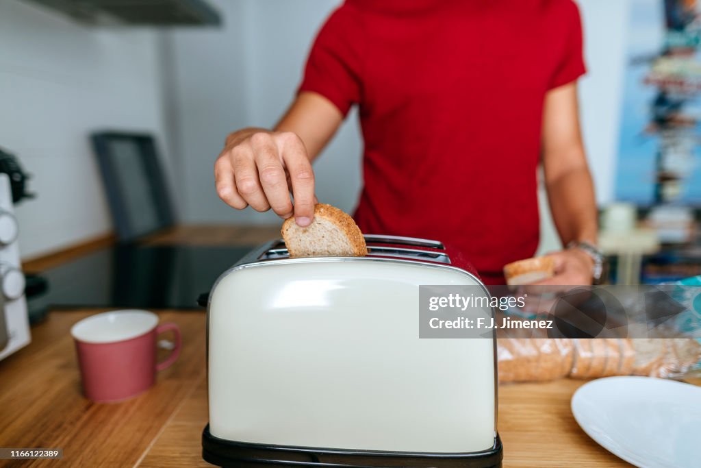 Close-up of man toasting bread with toaster in kitchen