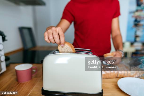close-up of man toasting bread with toaster in kitchen - toaster stock pictures, royalty-free photos & images