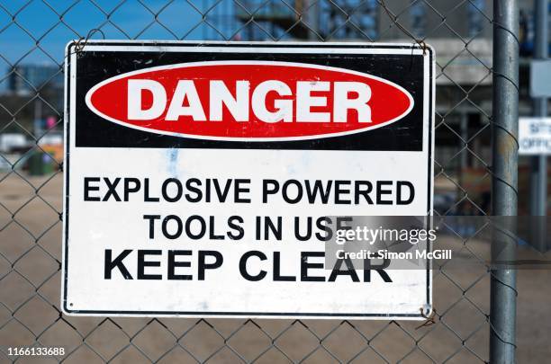 'danger: explosive powered tools in use. keep clear' warning sign on a wire mesh fence around a construction site - bombers stock pictures, royalty-free photos & images